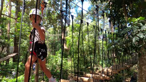 a young little girl walks across a bridge at a zipline adventure park for kids