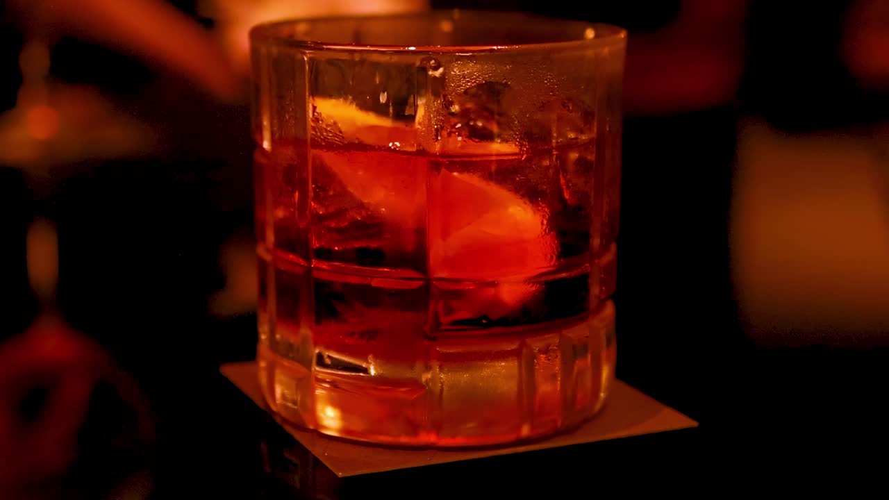 Close-up of a hand holding a cocktail glass with ice and an orange slice in dim lighting.