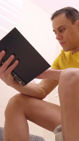 man reading a book while sitting on the toilet