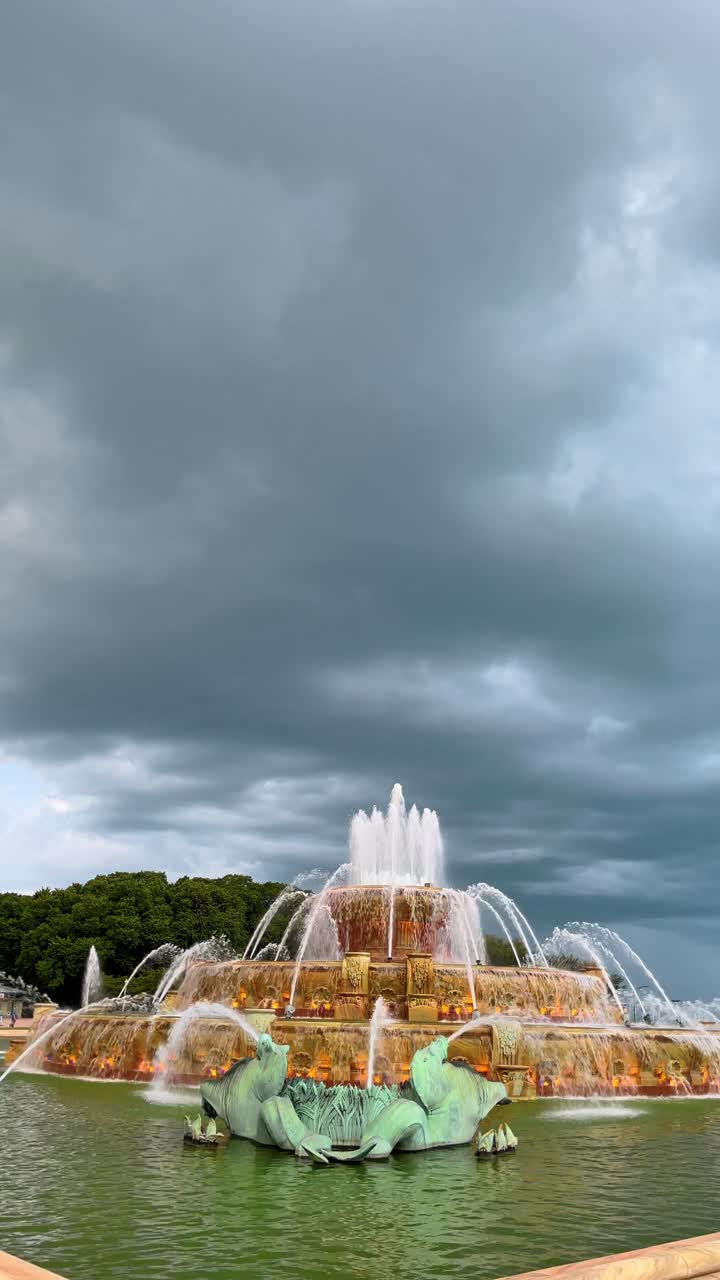 Fontana di Buckingham a Chicago sotto drammatiche nuvole temporalesche. Ampia inquadratura della storica Fontana di Buckingham a Grant Park, Chicago, con getti d'acqua attivi sotto un cielo scuro.