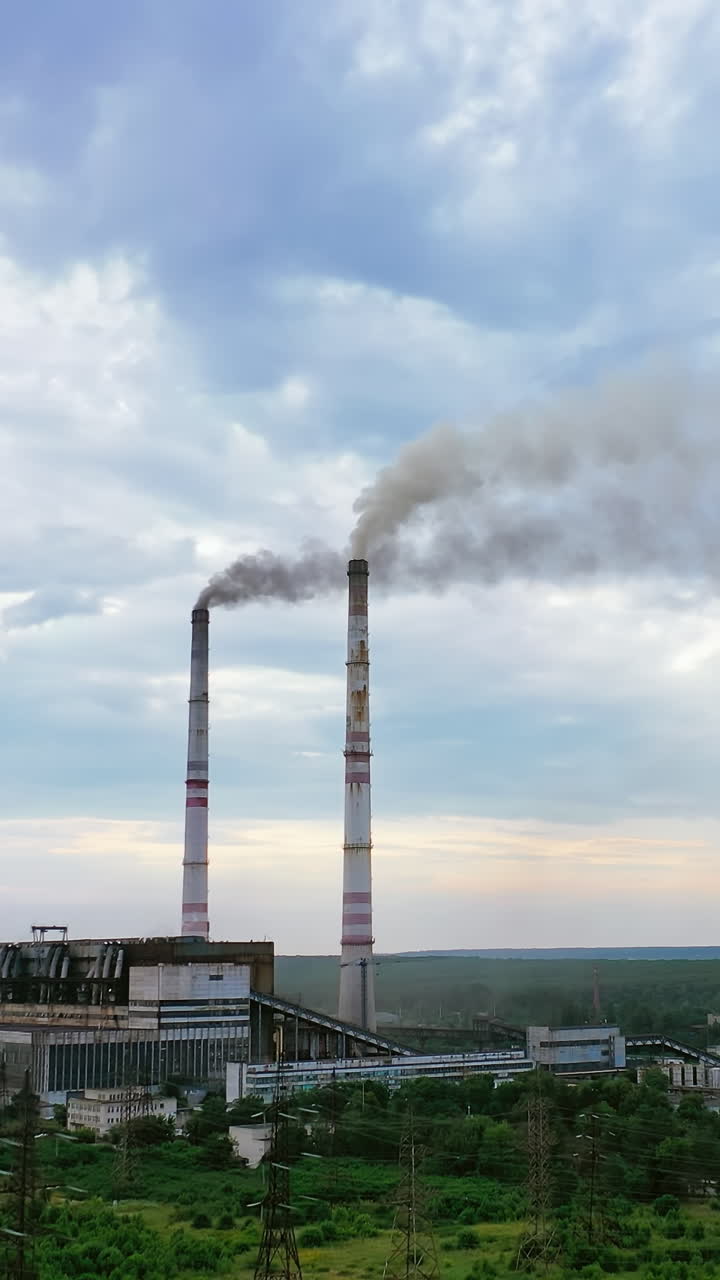 Industrial plant releases toxic emissions into the air. Smoke clubs come out of chimneys on a background of the sky. Nature in danger. Vertical video