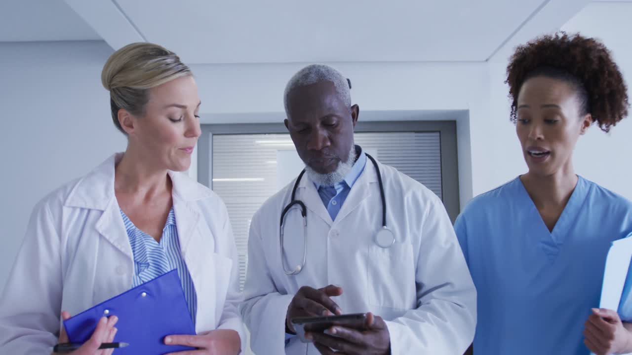 Diverse male and female doctors and medical staff standing in hospital corridor looking at tablet