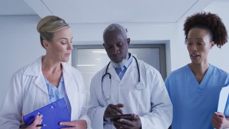 diversos médicos masculinos y femeninos y personal médico de pie en el pasillo del hospital mirando la tableta