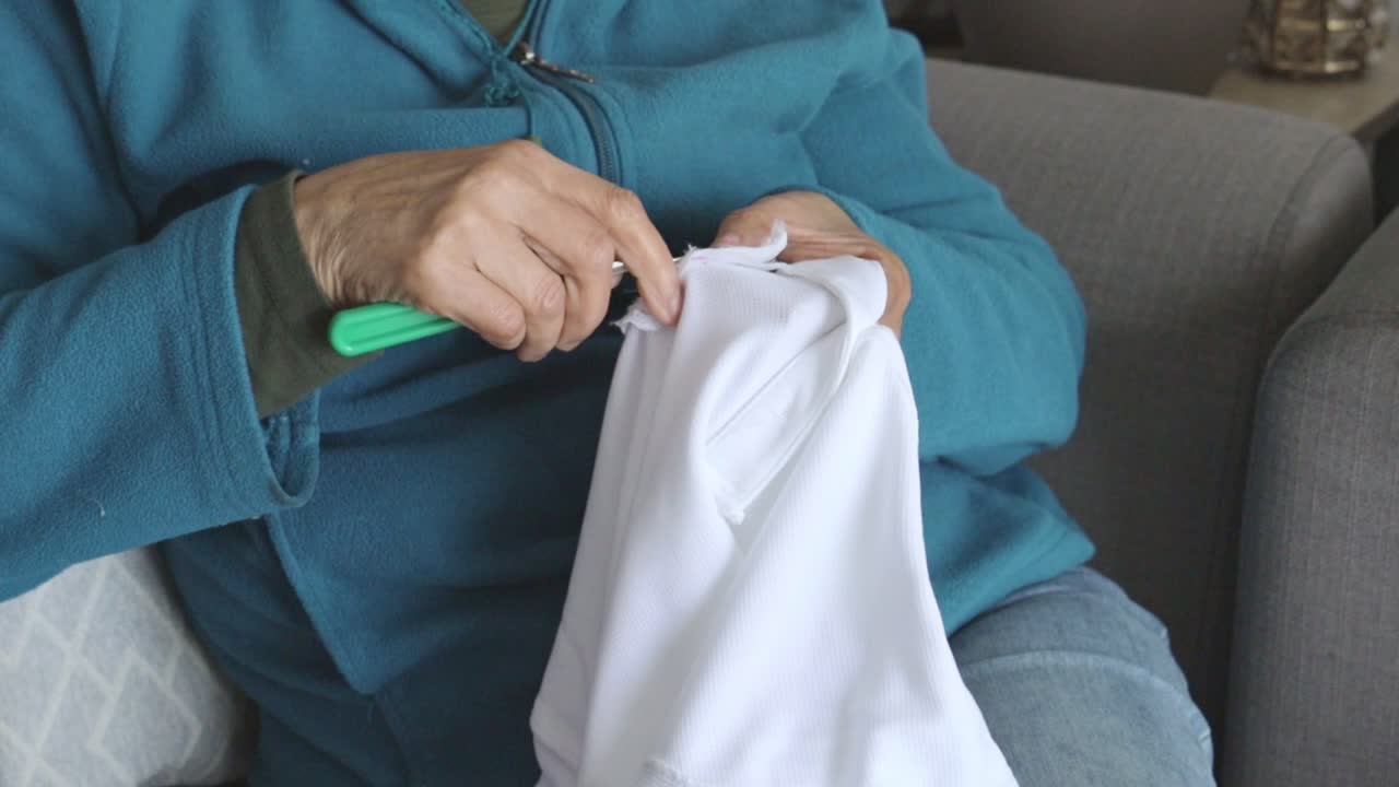Primo piano di mani che usano uno scucitore su tessuto bianco