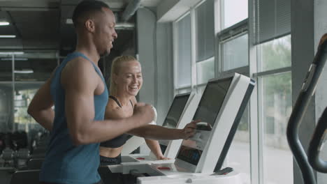 Side-view-of-caucasian-female-monitor-and-an-athletic-african-american-man-in-the-gym.