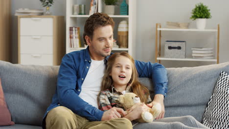 Teenage-Pretty-Blonde-Girl-Sitting-And-Hugging-Her-Teddy-Bear-While-Her-Father-Hugging-Her-And-They-Talking