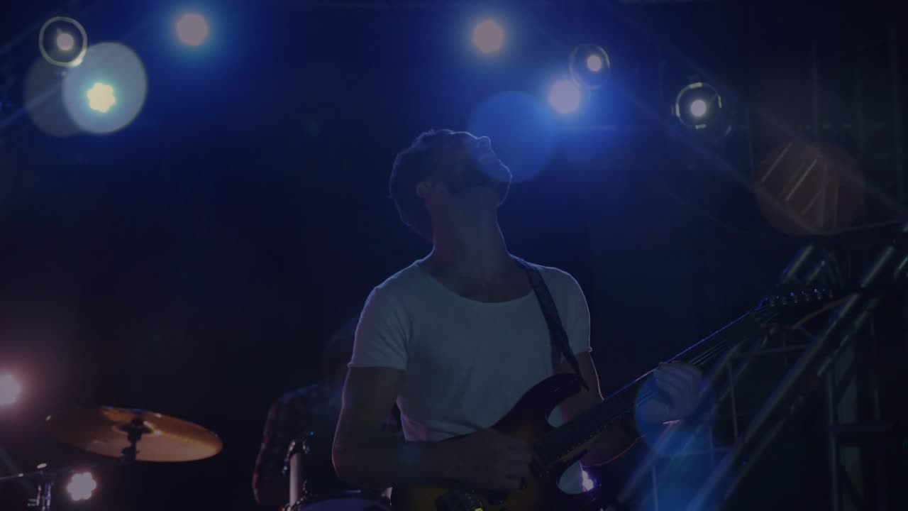 Chitarrista che impugna la chitarra e strimpella accordi sul palco, alimentando il ritmo della band con luci tremolanti.