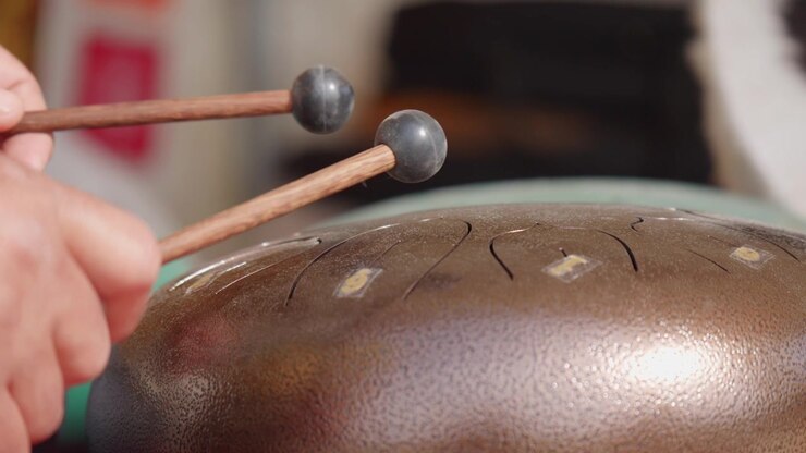 Close-up of hands playing a steel tongue drum with wooden mallets, creating a relaxing percussive performance with melodic and meditative tones.