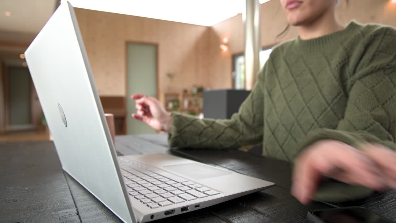 Woman in cozy sweater using smartphone and drinking coffee at home office