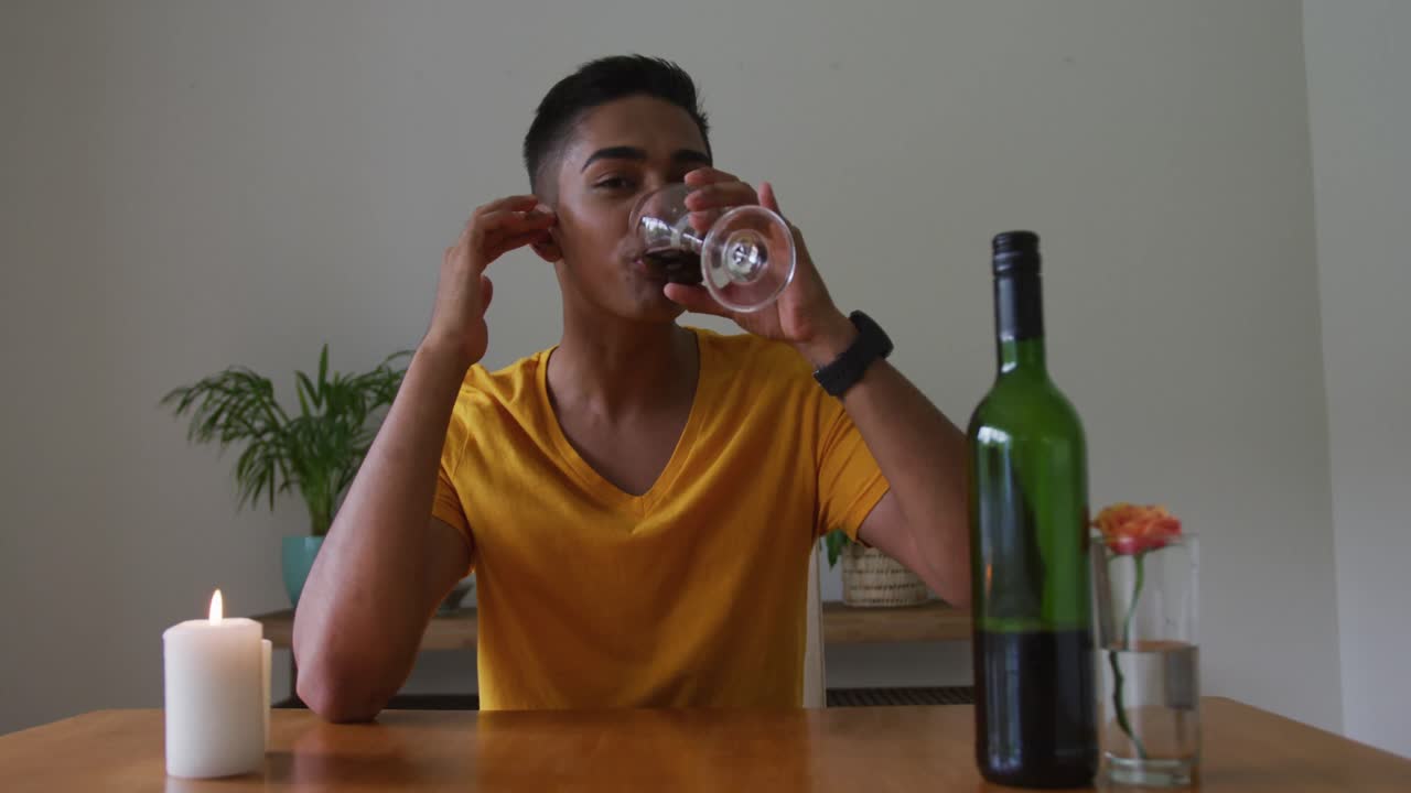 hombre de raza mixta sonriente sentado en la mesa con una vela encendida bebiendo vino tinto