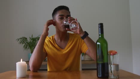 Smiling-mixed-race-man-sitting-at-table-with-lit-candle-drinking-red-wine