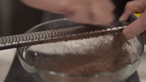 A-young-girl-grates-chocolate-into-a-bowl-for-melting-while-making-millionaire-shortbread-cookies-while-wearing-safety-gloves-5