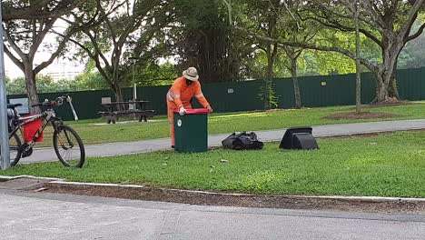 cleaner with face mask clearing dustbin during covid-19 lockdown in singapore, asia
