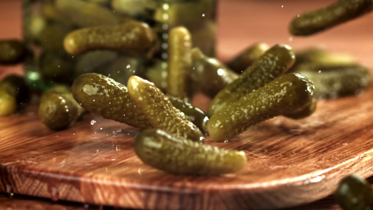 Ralenti de cornichons tombant sur une planche à découper en bois mouillée