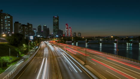 Timelapse-Del-Tráfico-Nocturno-En-La-Autopista-Olímpica-Daero-Con-Edificios-Del-Distrito-Financiero-De-Yeouido-Y-Vista-De-La-Torre-De-63-Edificios,-Tren-Subterráneo-Cruzando-El-Río-Han---Hiperlapso-Panorámico