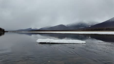 Flujo-Lento-De-Otra-Mitad-Del-Río-Congelado-Contra-El-Fondo-De-Un-Cielo-Gris-Y-Montañas-Nevadas-4k