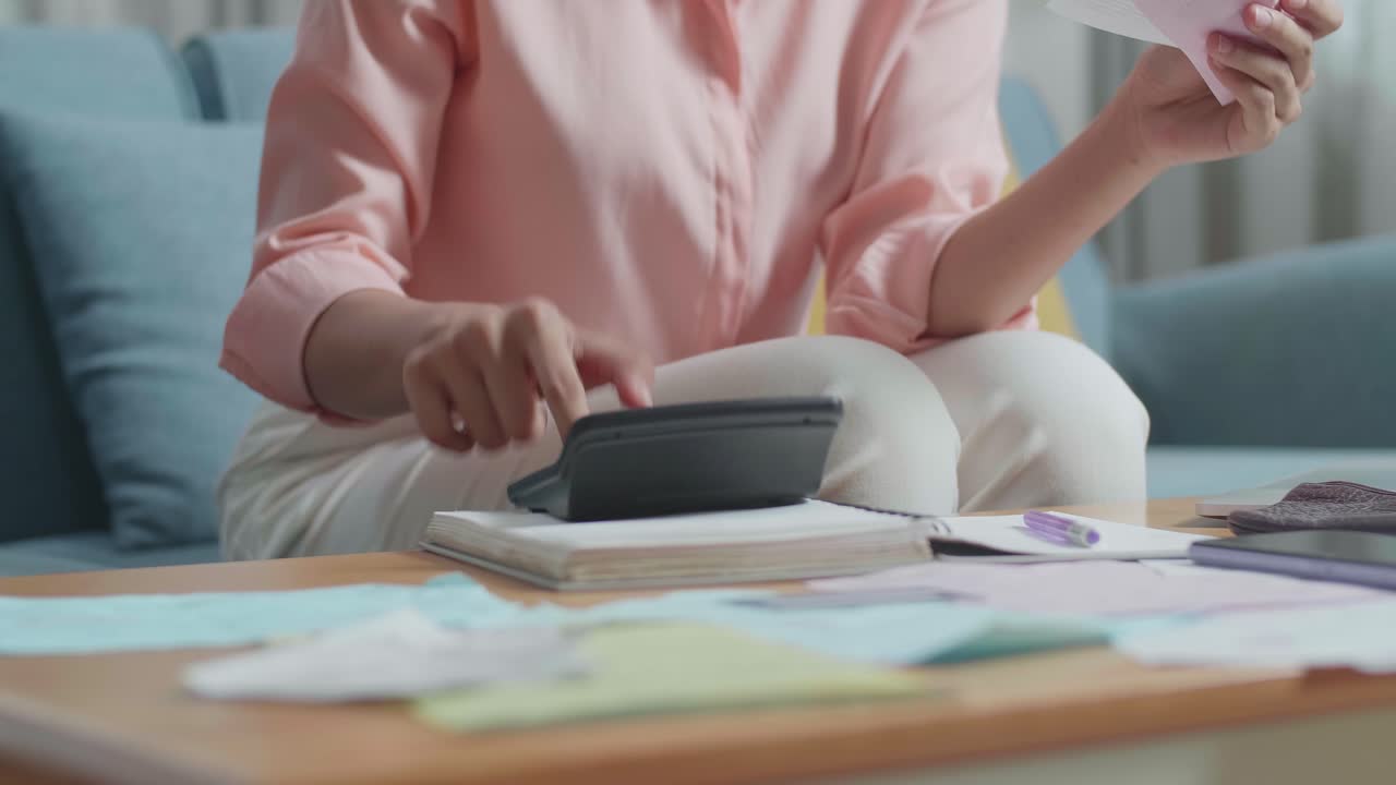 Primo piano di una donna asiatica turbata che tiene in mano una bolletta e una calcolatrice per calcolare l'importo a casa