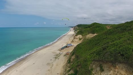 El-Parapente-Vuela-Sobre-La-Playa-Cerca-De-Las-Colinas,-Sigue-El-Dron