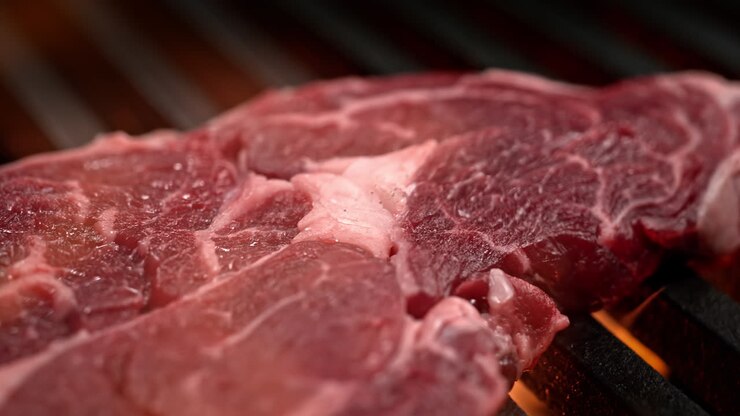 Raw Ribeye Steak Barbecuing On The Charcoal Grill Among Bursting Flames, BBQ in Macro and Slow Motion