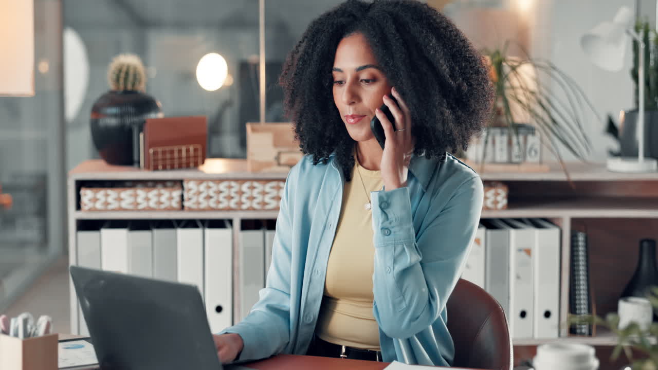 Professional woman working on laptop and taking a phone call in a modern office
