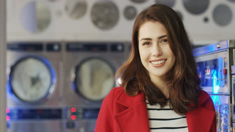 close up of beautiful young woman in red coat smiling cheerfully to camera in laundry service room