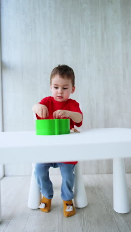 lovely four-year-old toddler sitting at desk busy with a toy. cute kid is focused on educational puzzle game. vertical video.