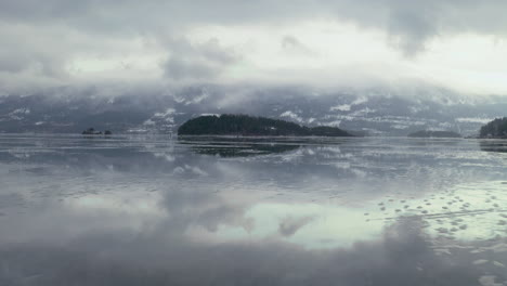 Drone-Flying-Above-Icy-Lake-With-Cloudy-Sky-Reflection