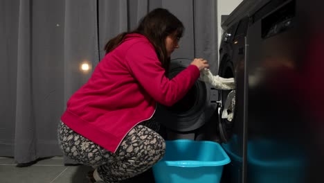 Pregnant woman doing laundry, bending to take baby clothes from washer indoors