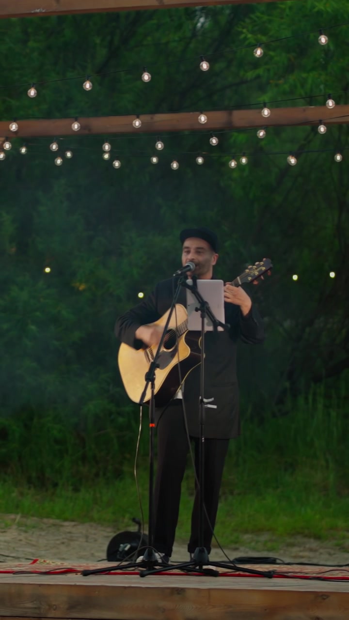 Mann spiller akustisk gitar og synger på utendørsscene