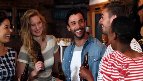 Smiling-group-of-friends-interacting-while-having-bottle-of-beer