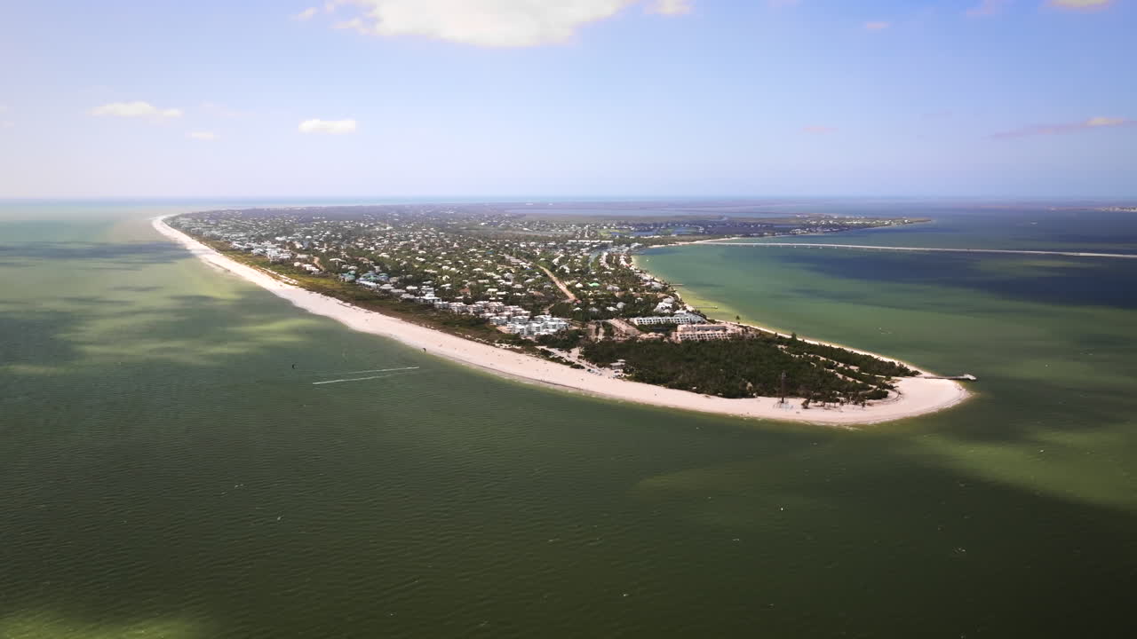 Filmový, vysoko letící širokoúhlý letecký záběr dronem kroužící nad oceánskou stranou historického majáku na ostrově Sanibel a východního cípu ostrova Sanibel na Floridě, s jasným pobřežím.