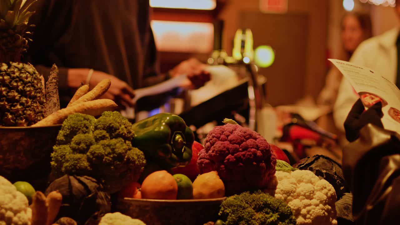 Scatto fotografico di una cassa di ristorante con verdure fresche in primo piano e un pagamento di un cliente sullo sfondo, in un ambiente di alimentazione sana