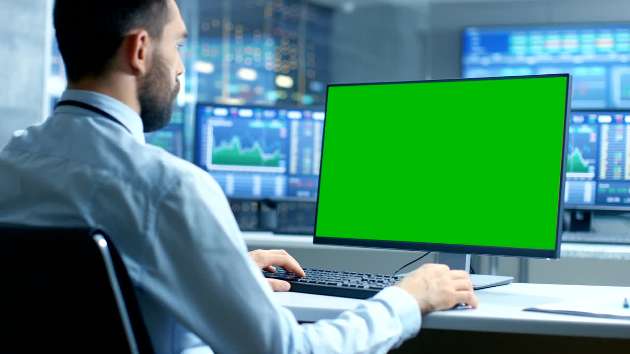 más de la vista del hombro del comerciante del mercado de valores que trabaja en una computadora con una pantalla verde de maqueta aislada. en el fondo los monitores muestran números y gráficos de cotización de acciones.