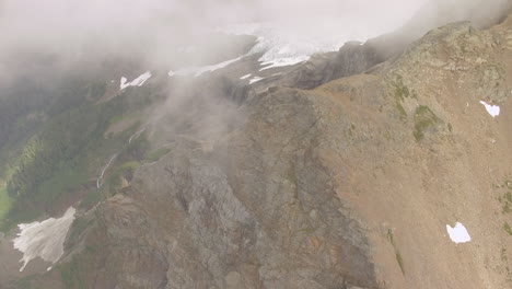 slow panning look down a mountain top and sheer cliffs onto a meadow and lake below