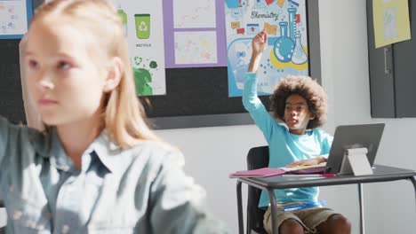 Video-of-diverse-schoolchildren-at-desks-with-tablets,-raising-hands-to-answer-in-class,-copy-space