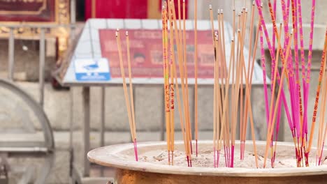 colorful incense sticks stand upright in a circular holder, set against a temple backdrop.