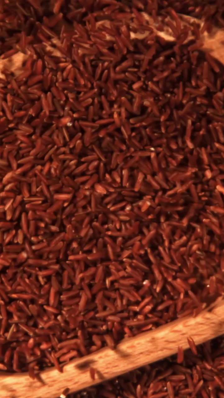 Slow Motion of Red Rice Grains Falling into a Wooden Spoon