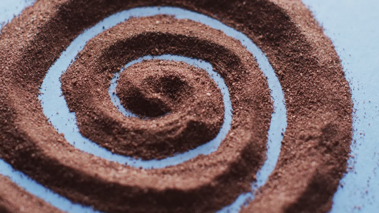 Video of close up of brown sand grains and copy space in swirl on blue background