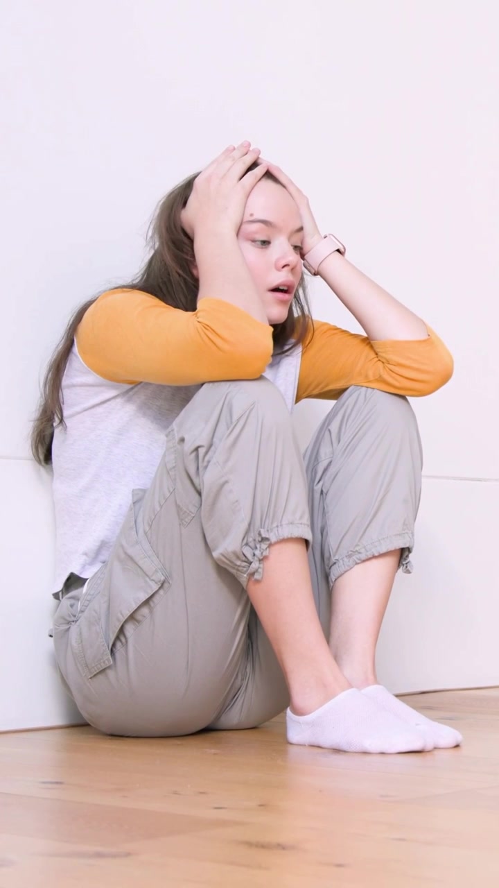 Video verticale: Donna in pantaloni a terra che si tiene le tempie con le mani, cercando sollievo.