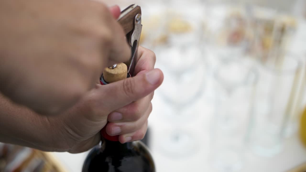 Mano caucasica che apre una bottiglia di vino rosso con un cavatappi e tappo di sughero vero, con il catering sullo sfondo
