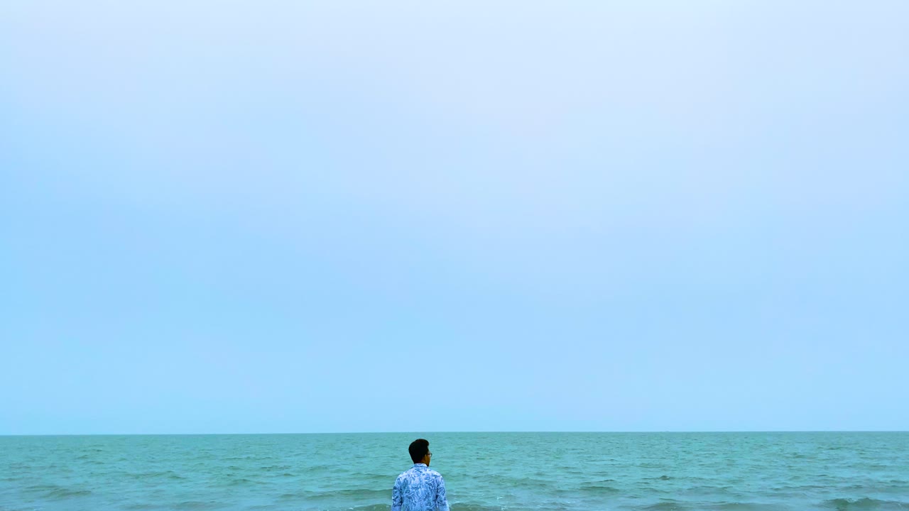 Man standing alone on sea shore enjoying vast ocean view under blue sky. Minimalistic view