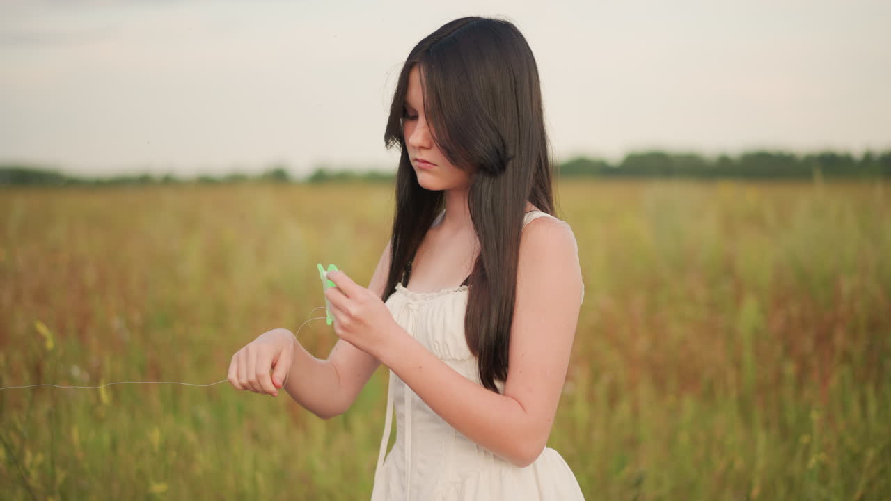 초원에서 녹색 종이를 접고, 가장자리를 검사하며, 꽃집 주인이자 몽상가처럼 리본을 꿰는 백인 여성, 부드러운 금빛 조명, 키 큰 풀, 야생화 장식, 촉각적인 슬로 모션, 친밀한 분위기