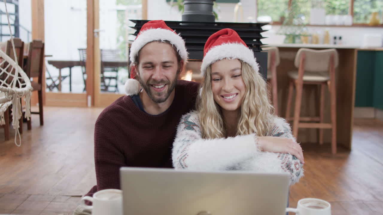una pareja con sombreros de papá noel usando una computadora portátil para una llamada de video de navidad, en cámara lenta
