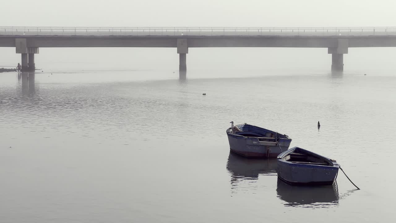 Two moored boats against the backdrop of a foggy bridge