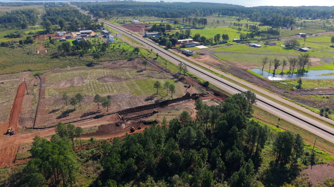 Aerial clip focuses on active construction site near highway, with bulldozers carving through terrain under bright skies. Ideal for civil engineering content.