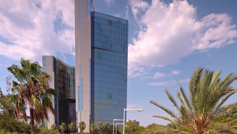 barcelona mirrored glass skyscraper with clouds in the sky and wind blowing palm trees