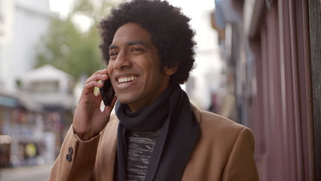 young man using phone as he walks along busy city street