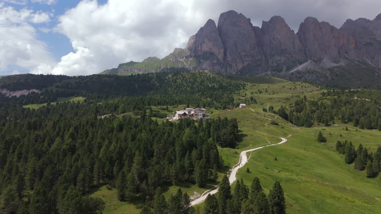 impresionante vista aérea de la cabaña de regensburger enclavada entre exuberantes colinas verdes, con los altos picos de seceda en las dolomitas que proporcionan un telón de fondo impresionante