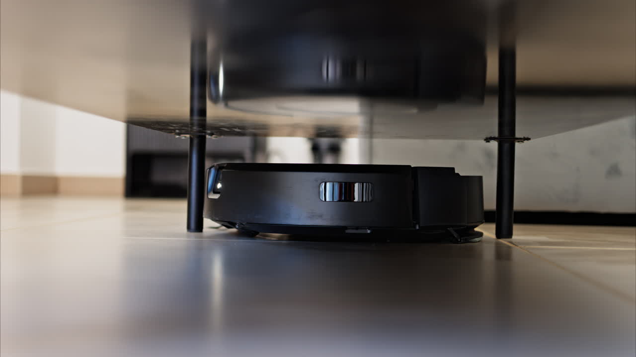 Close up of a small, black robot vacuum cleaning under surfaces in the house