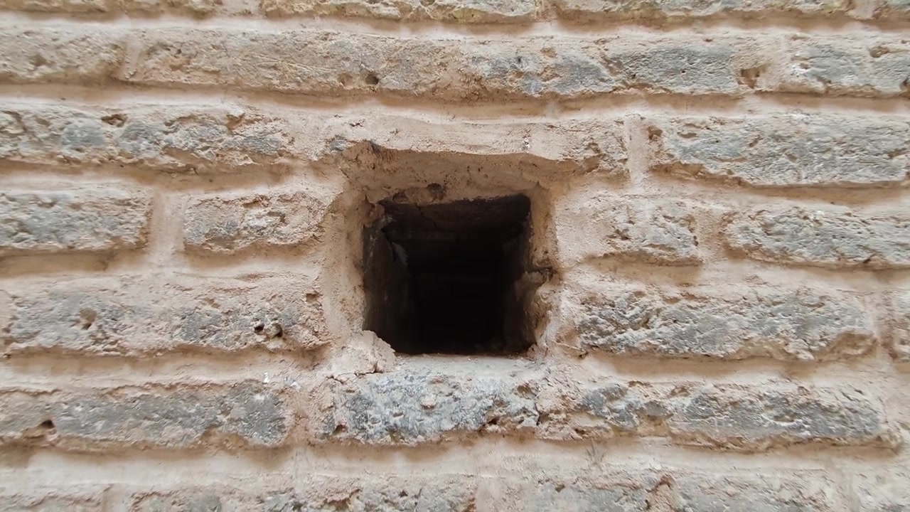 Telecamera che si allontana da un piccolo foro quadrato in un antico muro di mattoni